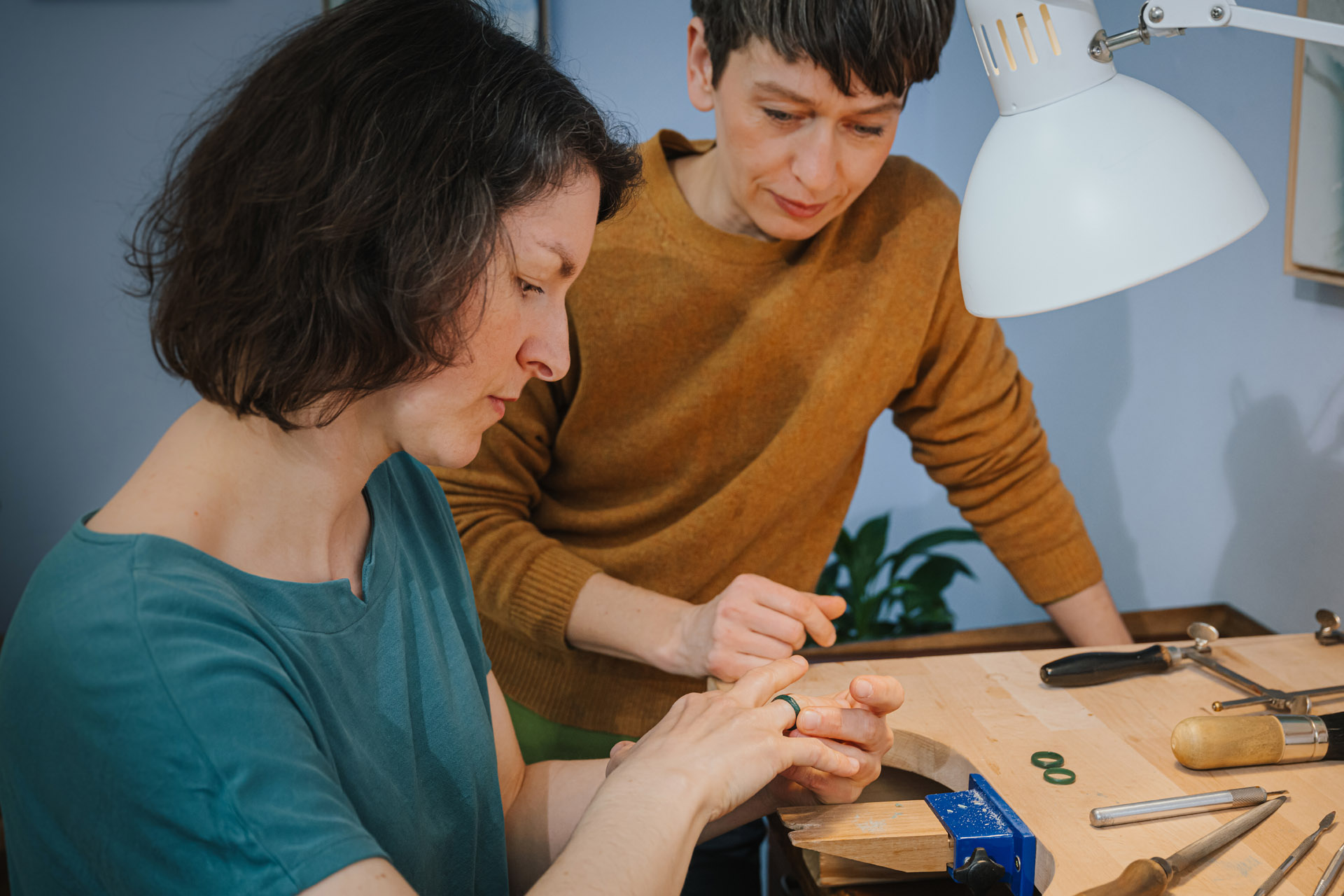 Zwei Personen nehmen an einem Goldschmiede Schmuckkurs / Trauringkurs in der Schmuckwerkstatt Schimmer Goldschmiede in Halle /Saale bei Annekathrin Pohle Sophie Baumgärtner, Charlotte Antony teil. Die Frau im grünen Oberteil wird von der Kursleiterin beraten.